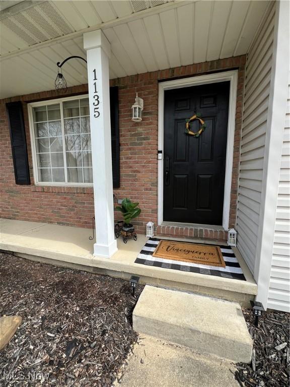 property entrance featuring covered porch and brick siding