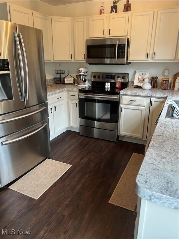 kitchen featuring stainless steel appliances, light stone countertops, dark wood-style floors, and white cabinetry