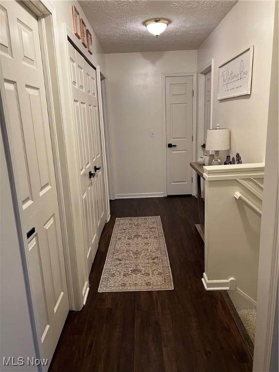 hall featuring a textured ceiling, baseboards, and dark wood finished floors