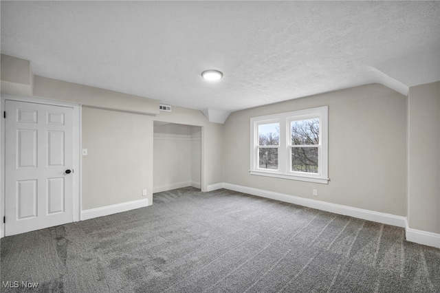 unfurnished bedroom with a textured ceiling, a closet, visible vents, carpet floors, and lofted ceiling