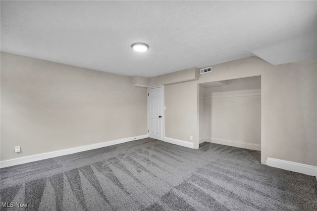 interior space with visible vents, baseboards, a closet, dark carpet, and a textured ceiling