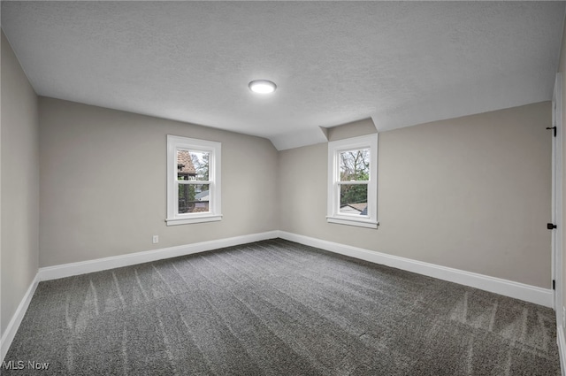 interior space featuring dark colored carpet, baseboards, a textured ceiling, and lofted ceiling
