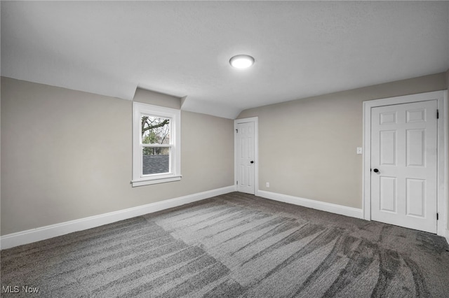 empty room featuring baseboards, vaulted ceiling, and carpet