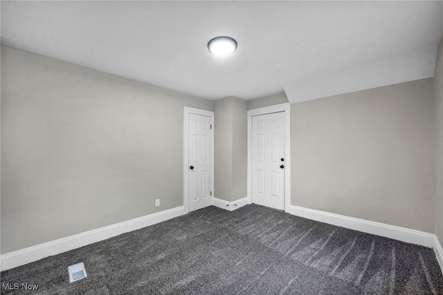spare room with baseboards and dark carpet