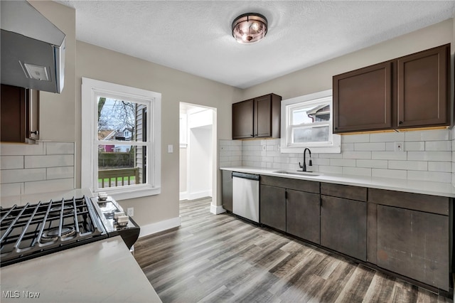 kitchen featuring light countertops, dark brown cabinets, dishwasher, a sink, and wood finished floors