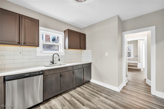 kitchen with stainless steel dishwasher, light wood-style flooring, tasteful backsplash, light countertops, and a sink