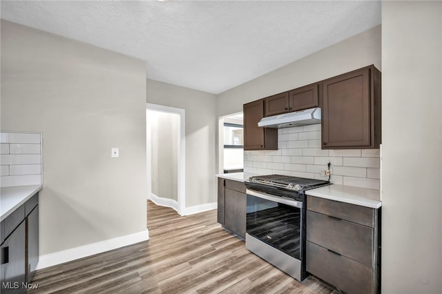 kitchen with stainless steel gas stove, dark brown cabinetry, tasteful backsplash, under cabinet range hood, and light countertops