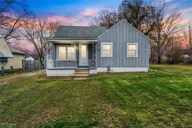 bungalow with a front yard, covered porch, board and batten siding, fence, and roof with shingles