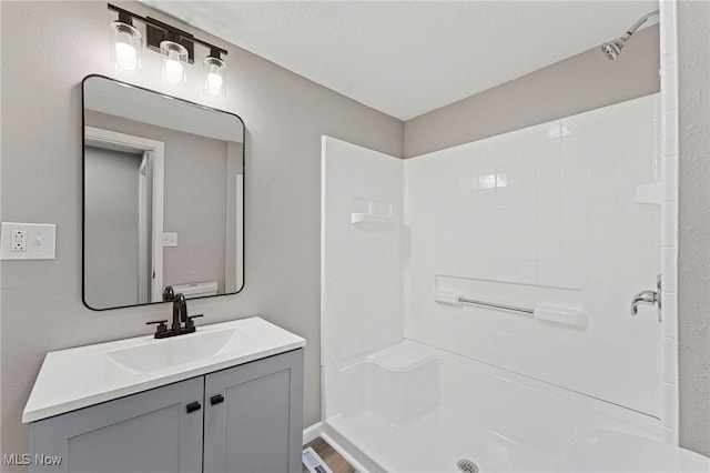 full bathroom featuring a textured ceiling, vanity, and walk in shower
