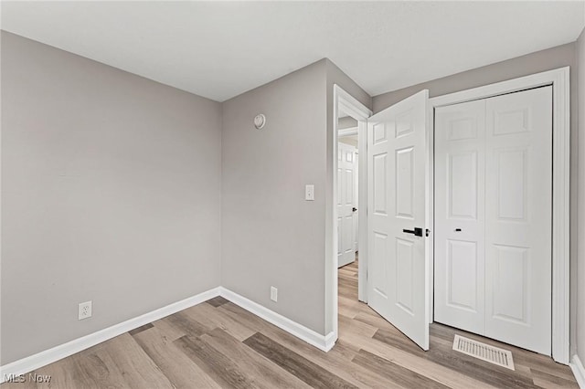 unfurnished bedroom featuring a closet, visible vents, baseboards, and wood finished floors