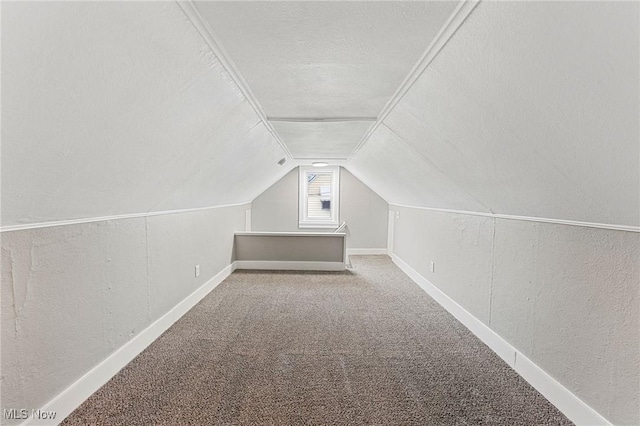 additional living space with baseboards, vaulted ceiling, a textured wall, a textured ceiling, and carpet floors