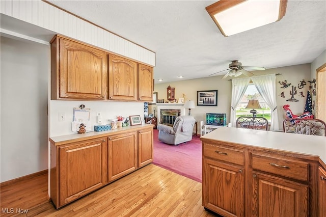 kitchen featuring light wood-style flooring, light countertops, a fireplace, and a ceiling fan
