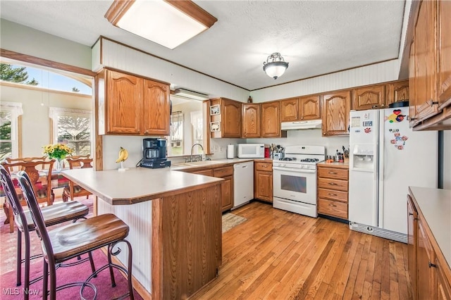 kitchen featuring white appliances, brown cabinetry, light wood-type flooring, under cabinet range hood, and a sink