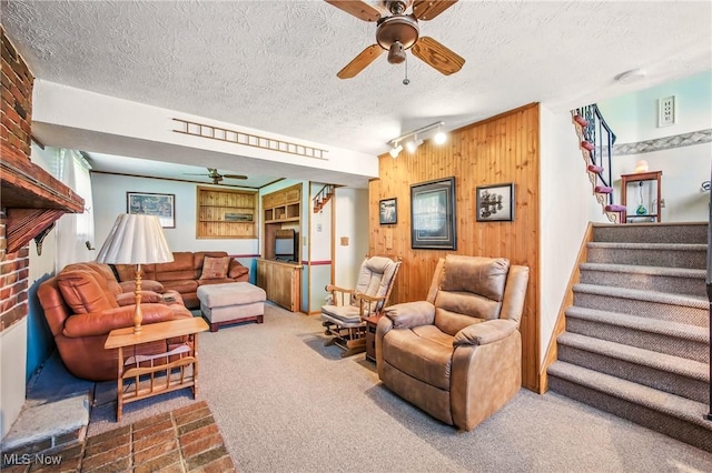 living area featuring rail lighting, stairway, wooden walls, a textured ceiling, and a ceiling fan