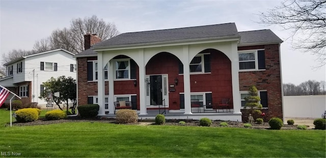 view of front facade featuring brick siding, a porch, a front lawn, and a chimney