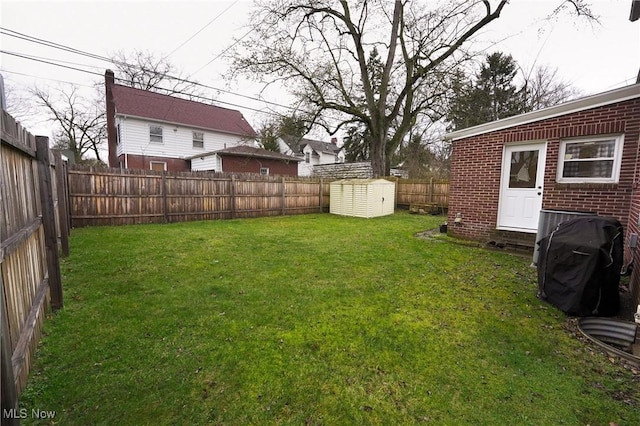 view of yard with entry steps, a fenced backyard, an outdoor structure, and a storage shed