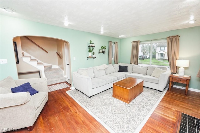 living room with arched walkways, a textured ceiling, wood finished floors, stairs, and baseboards