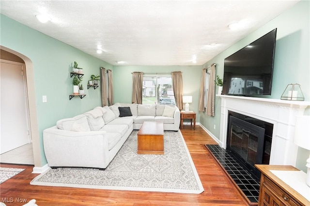 living room with arched walkways, a fireplace with flush hearth, baseboards, and wood finished floors