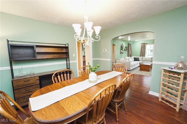 dining space with arched walkways, wood finished floors, a notable chandelier, and a textured ceiling