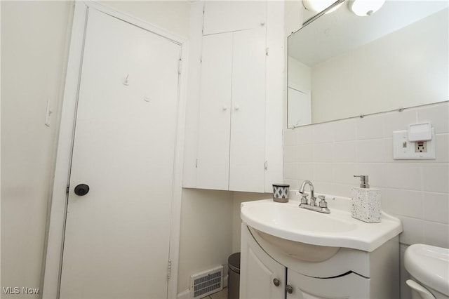 half bathroom with vanity, visible vents, tile walls, and toilet