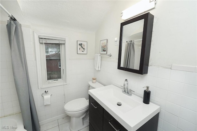 full bathroom with vanity, tile patterned flooring, a textured ceiling, a wainscoted wall, and toilet