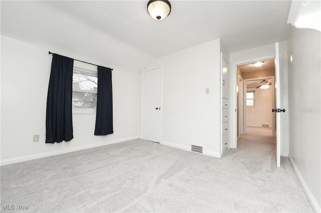 unfurnished bedroom with visible vents, baseboards, light carpet, and lofted ceiling