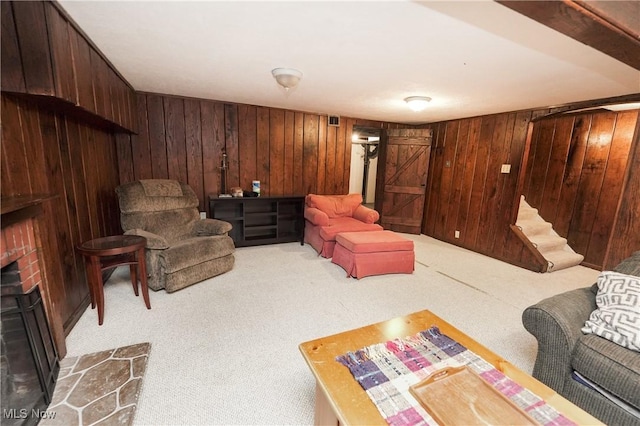 carpeted living room featuring visible vents, wood walls, stairway, and a brick fireplace