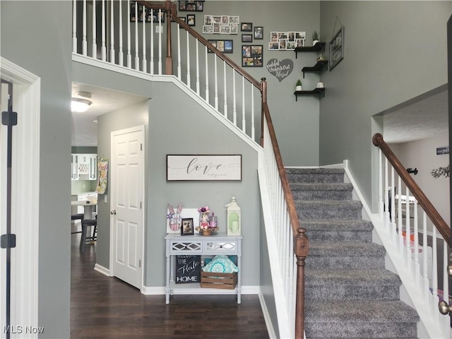 staircase featuring baseboards, a high ceiling, and wood finished floors