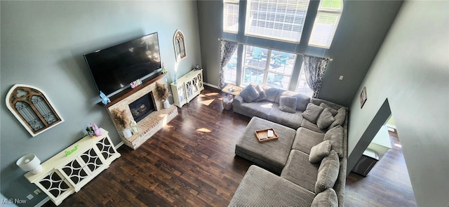 living room featuring a stone fireplace, plenty of natural light, a high ceiling, and wood finished floors