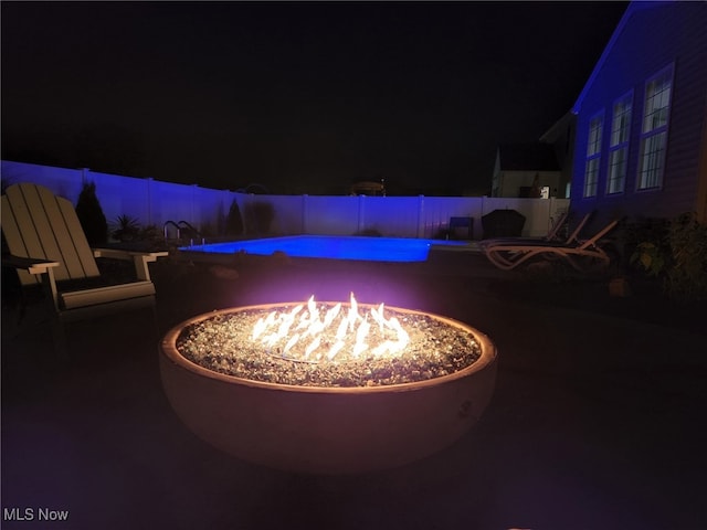 patio at twilight featuring an outdoor fire pit, a fenced in pool, and fence