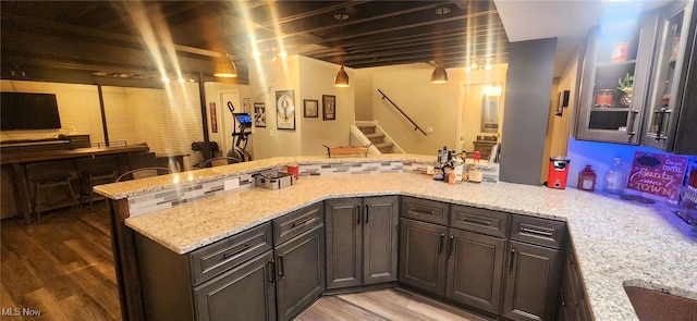 kitchen with light wood-style flooring, a peninsula, light stone counters, and glass insert cabinets