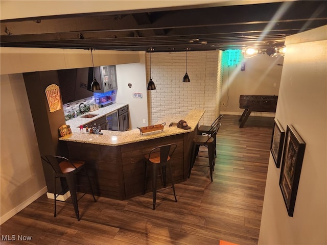 bar featuring indoor wet bar, baseboards, brick wall, dark wood finished floors, and a sink