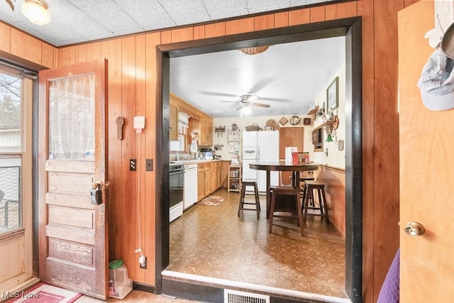 kitchen with wood walls, white appliances, visible vents, and ceiling fan