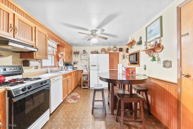 kitchen with light floors, white appliances, a wainscoted wall, ceiling fan, and a sink