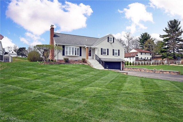 view of front facade with a chimney, aphalt driveway, a garage, and a front yard