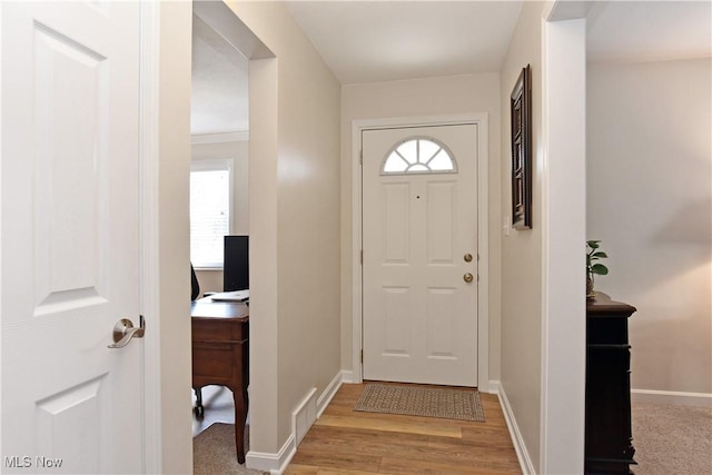 doorway with light wood-type flooring, visible vents, and baseboards