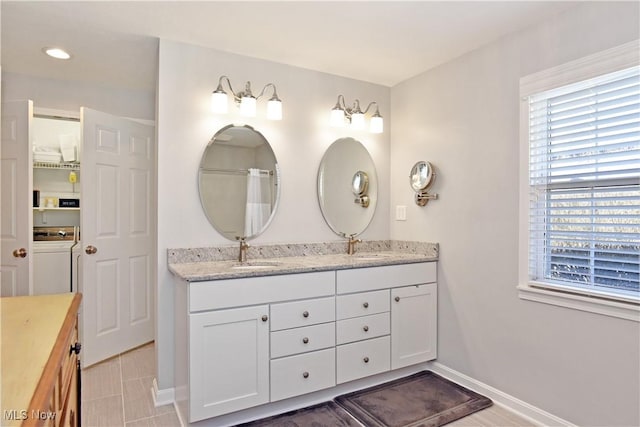 full bathroom with a wealth of natural light, double vanity, baseboards, and a sink