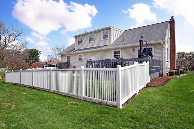 back of house featuring a yard, fence, a shingled roof, and a chimney