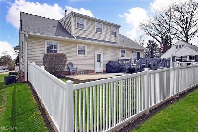 rear view of property with roof with shingles, a deck, a fenced backyard, and a lawn
