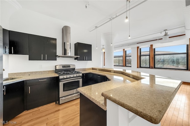 2077 E 4th St E Unit 4E, Cleveland, OH 44115 - kitchen with hanging light fixtures, wall chimney range hood, stainless steel gas range, dark cabinets, and light wood-style flooring
