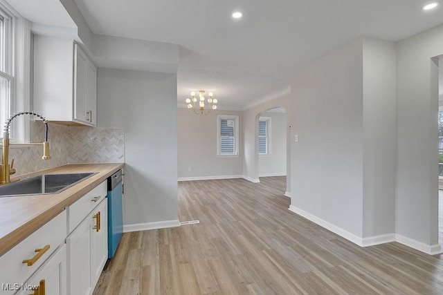 kitchen with light wood-style flooring, tasteful backsplash, arched walkways, dishwasher, and a sink