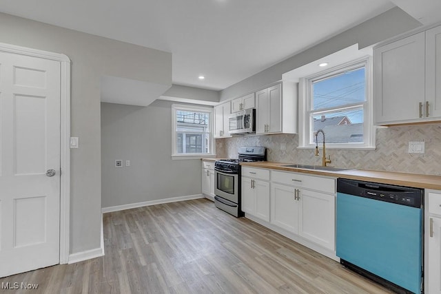 kitchen with white cabinetry, backsplash, stainless steel appliances, light wood finished floors, and a sink