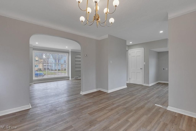 unfurnished room with arched walkways, recessed lighting, wood finished floors, baseboards, and a notable chandelier