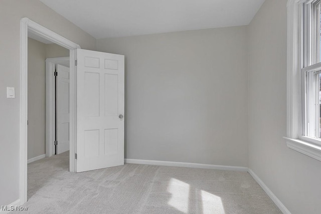 spare room with baseboards and light carpet