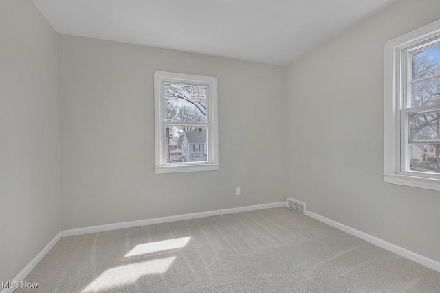 spare room featuring visible vents, light colored carpet, and baseboards