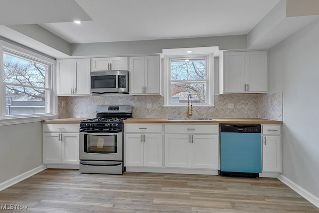 kitchen with butcher block countertops, appliances with stainless steel finishes, a sink, and baseboards