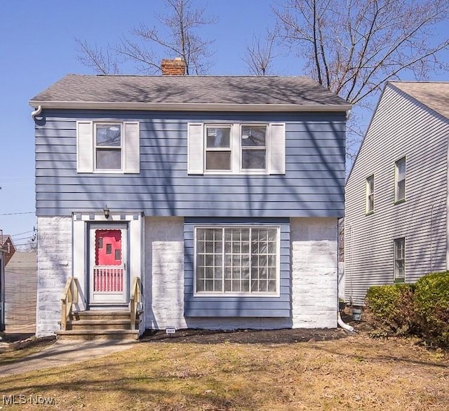 colonial-style house featuring entry steps, a chimney, and roof with shingles
