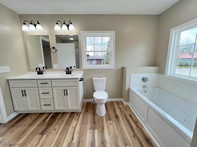 full bathroom with a garden tub, double vanity, a sink, and wood finished floors