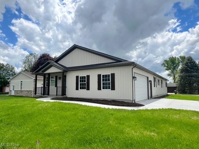 modern farmhouse with covered porch, a front yard, an attached garage, and driveway