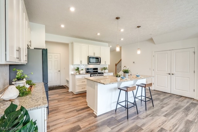 835-2 Dipper Ln, Aurora, OH 44202 - kitchen featuring appliances with stainless steel finishes, light wood finished floors, white cabinets, an island with sink, and a textured ceiling